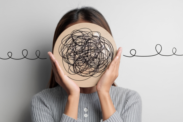 Woman holding a disc with a tangled scribble over her face, representing a mind too busy and tangled to relax